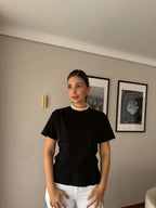 Mujer con camiseta entallada negra Alia de cuello redondo y jean blanco, vista frontal