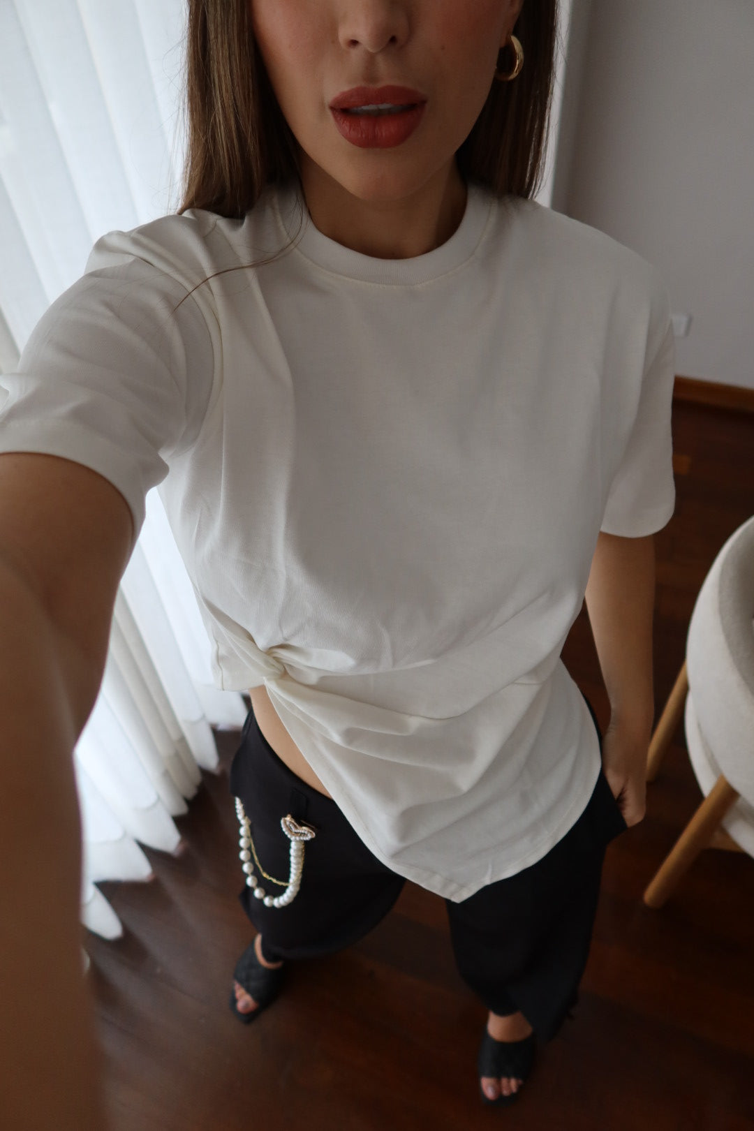 Mujer con camiseta Lucia blanca con nudo asimétrico y pantalón negro con cadena, foto en selfie